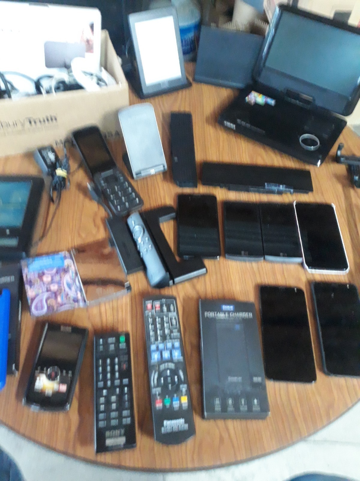 Table Full Of Miscellaneous Electronics Phones Chargers DVD Player Selfie Stick